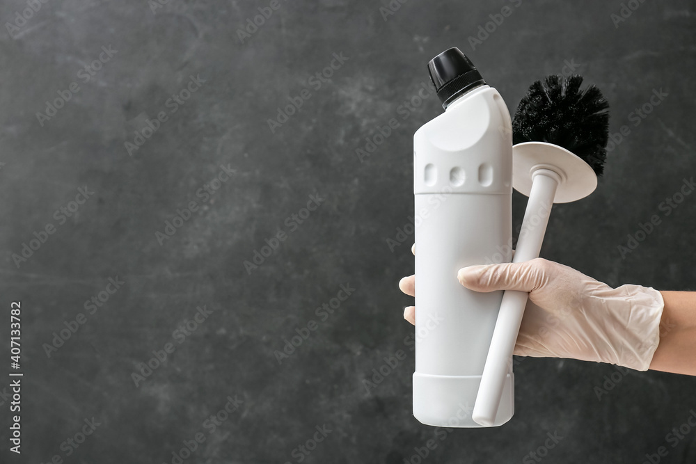 Hand in rubber glove with cleaning brush and detergent on dark background