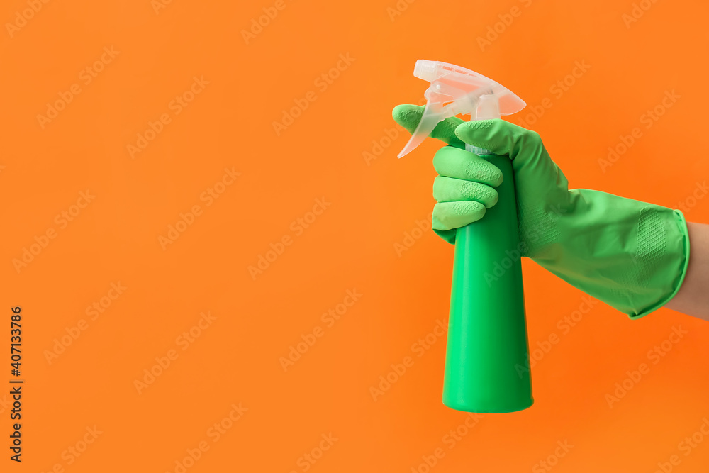 Hand in rubber glove with water sprayer on color background