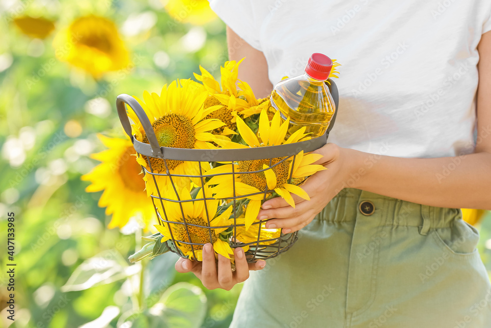 Woman holding basket with bottle of oil and sunflowers in field