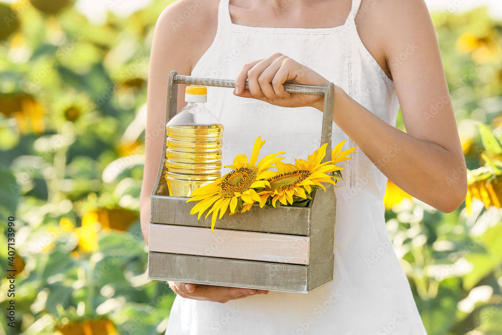 Woman holding basket with bottle of oil and sunflowers in field