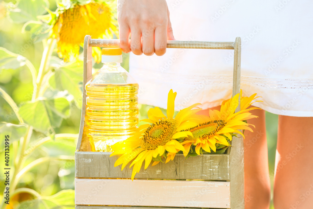 Woman holding basket with bottle of oil and sunflowers in field