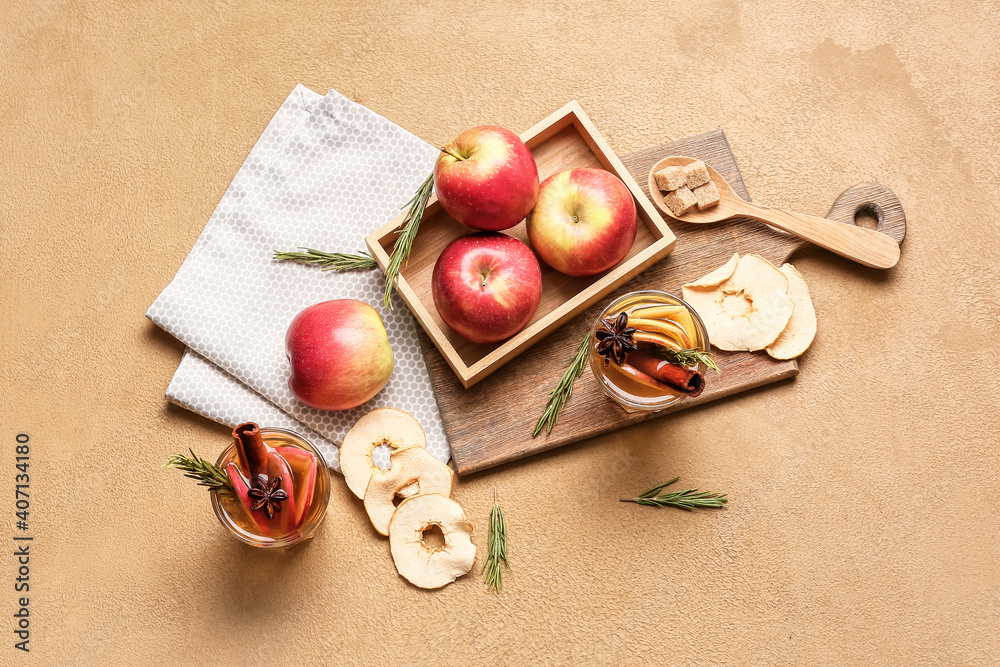 Tasty drink with spices and apple slices in glasses on color background