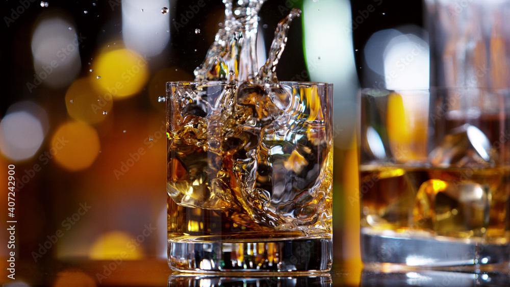 GLass of whisky with splashing liquid, bar on background