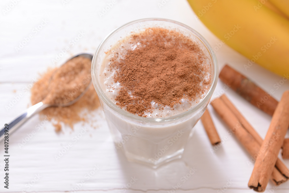 Tasty banana smoothie with cinnamon in glass on light background