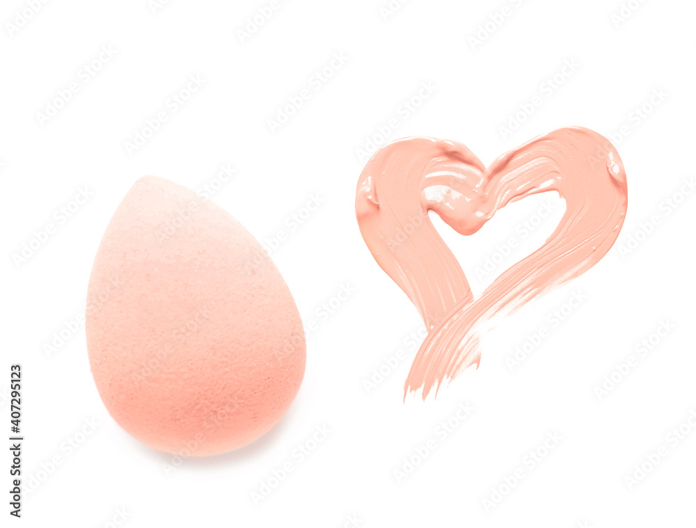 Sponge and heart made of makeup foundation on white background