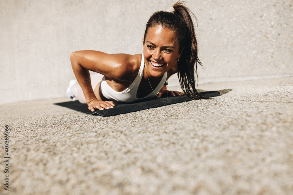 Smiling woman doing push ups on exercise mat