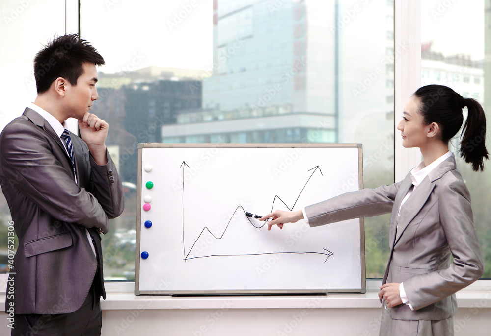 Businessman and businesswoman standing in front of line graph,pointing to line