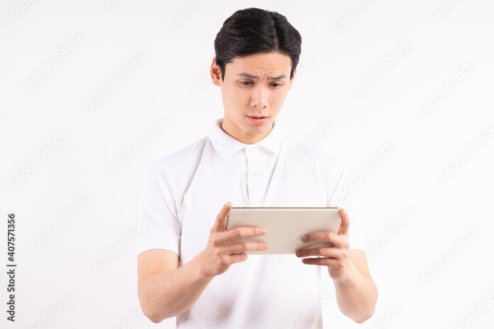 Cheerful young man standing on isolated white wall background. Stared at the tablet