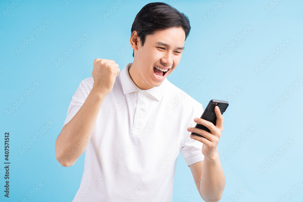 Excited handsome young male gamer playing online game on smartphone isolated on blue background