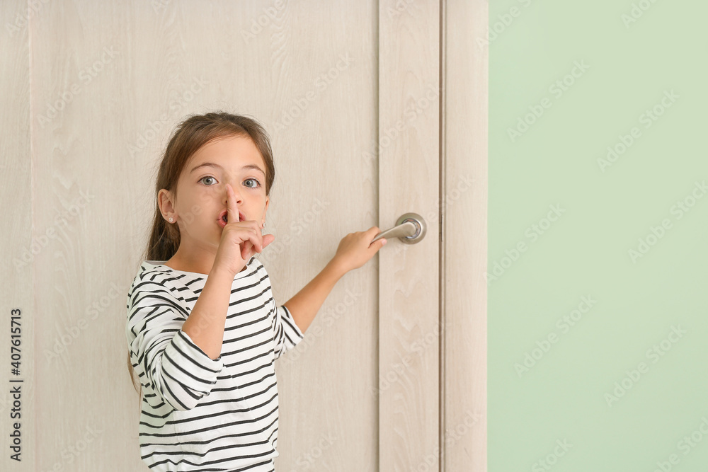 Cute little girl showing silence gesture near closed door