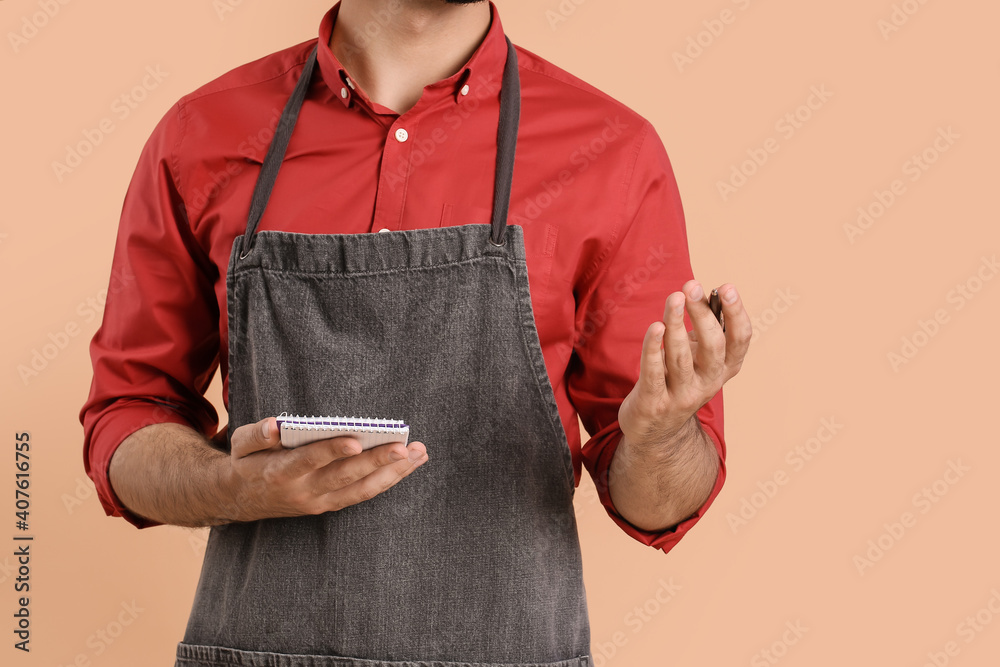 Young waiter with notebook on color background