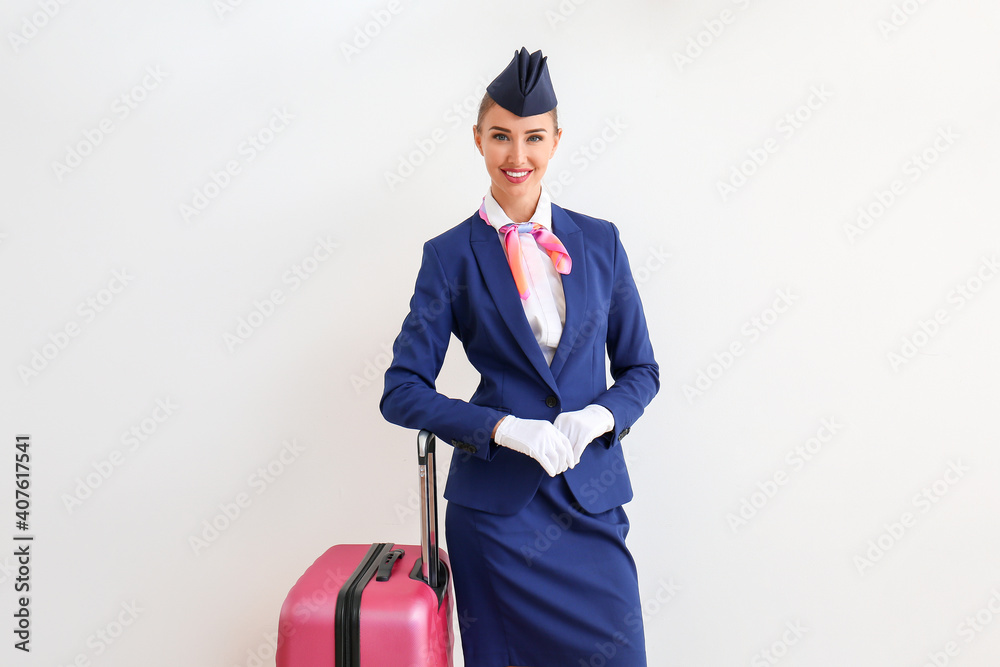 Beautiful stewardess with suitcase on light background