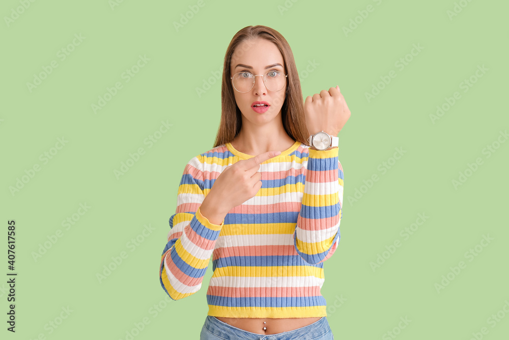 Stressed woman pointing on wristwatch on color background