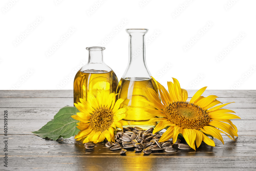 Bottles of oil, seeds and sunflowers on table against white background