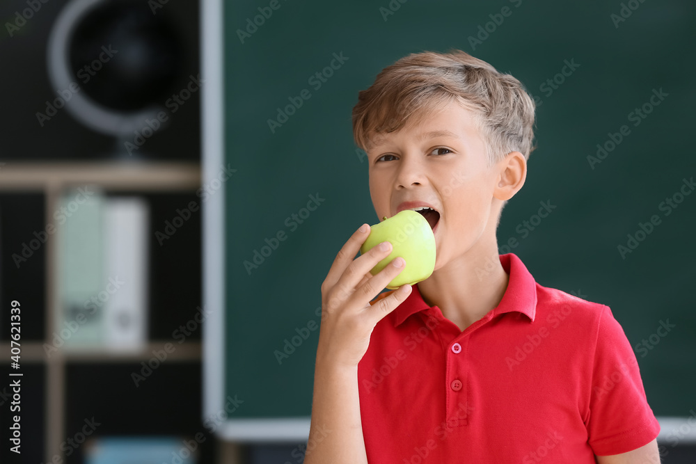 Schoolboy eating apple against blurred background in school