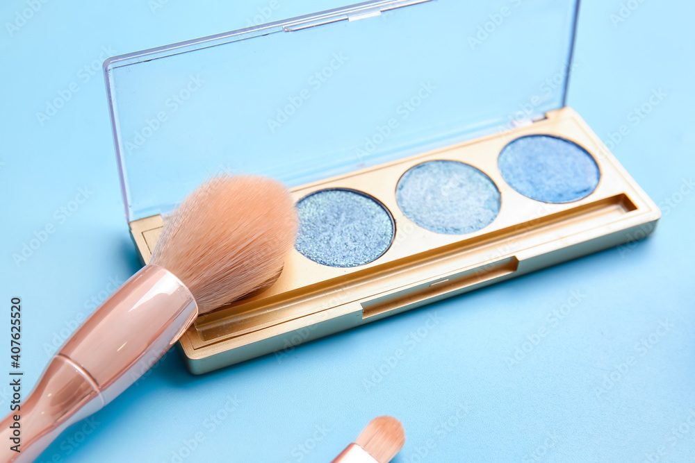 Makeup brush with cosmetics on color background