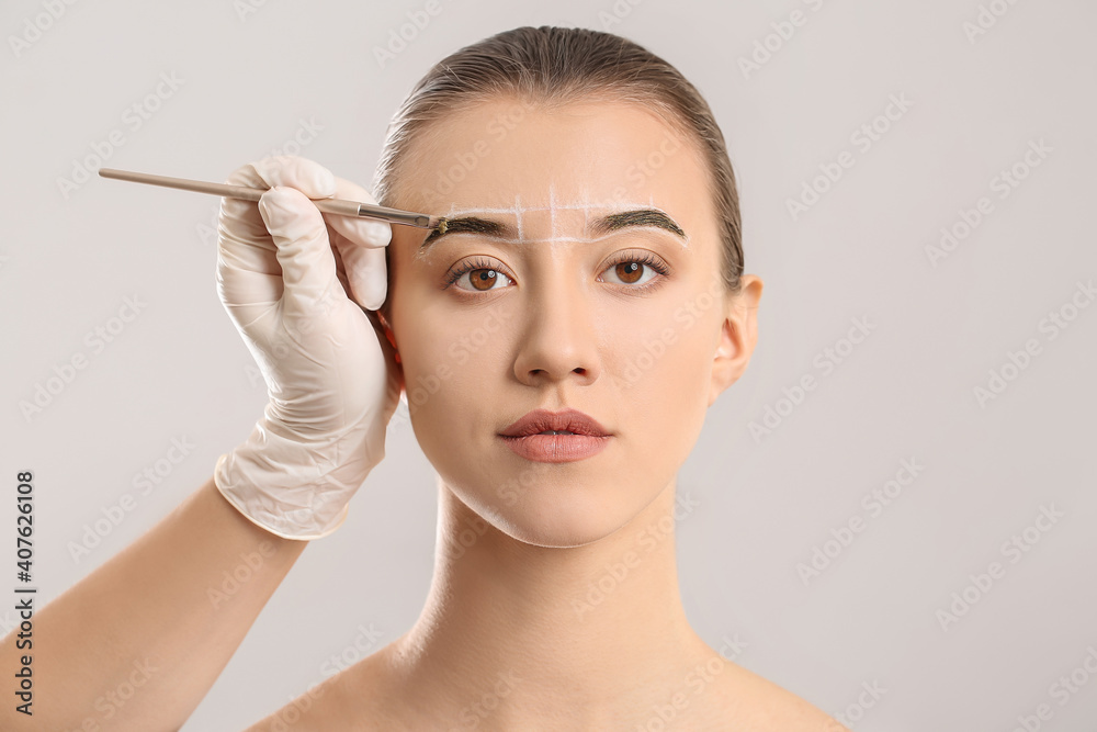 Young woman undergoing eyebrow correction procedure on grey background