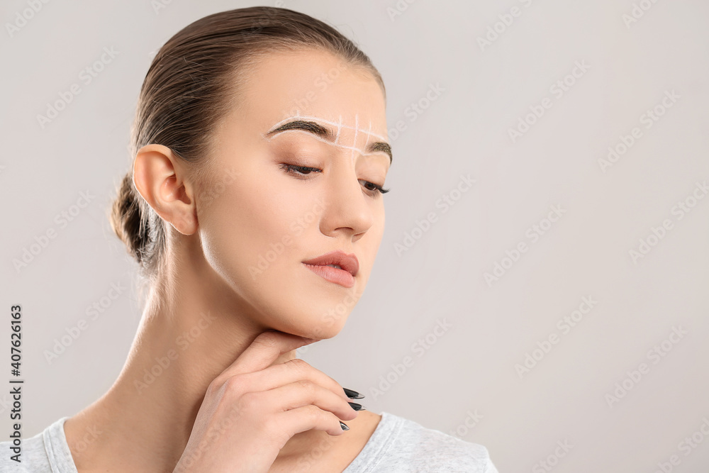 Beautiful young woman with marking for eyebrows correction against grey background