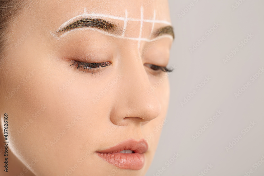 Beautiful young woman with marking for eyebrows correction against grey background, closeup