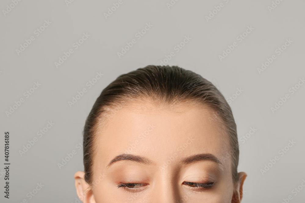 Young woman with beautiful eyebrows on grey background