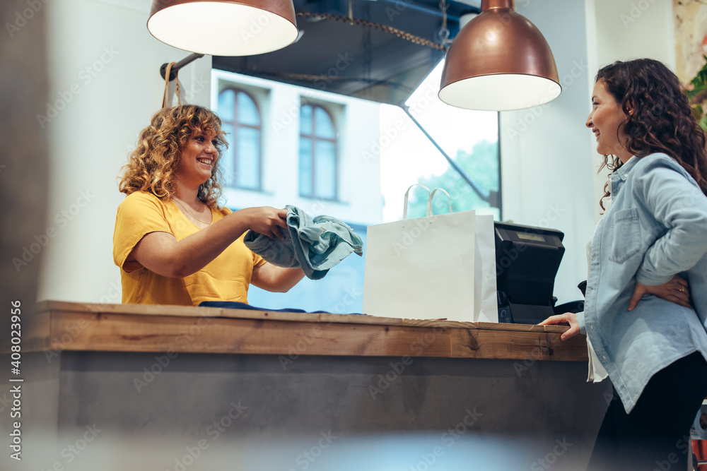 Saleswoman at shop pack purchases in shopping bag