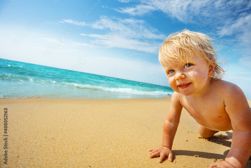 Close portrait of the crawling toddler with wondering smiling face expression on the sea beach