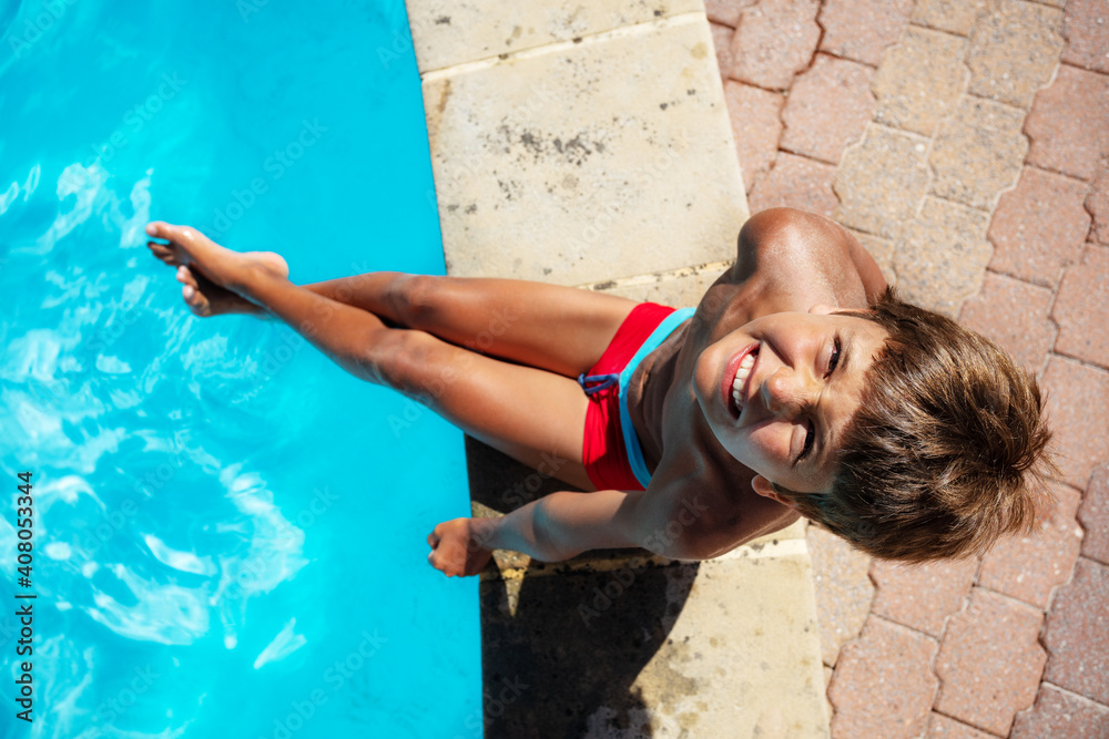 Photo of the ten years old boy sit on the side of the border of the swimming pool