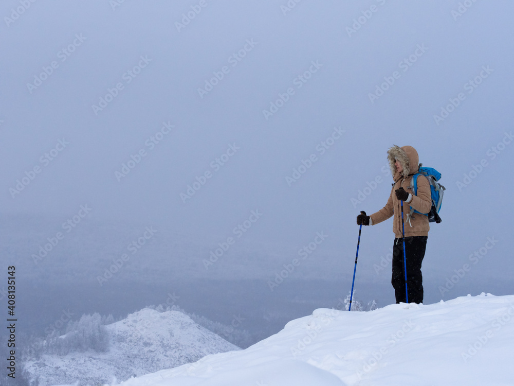 冬天，穿着暖和的外套，背着背包，带着滑雪杆在山上的雪地上徒步旅行。