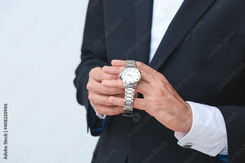 Young businessman holding stylish wristwatch on light background