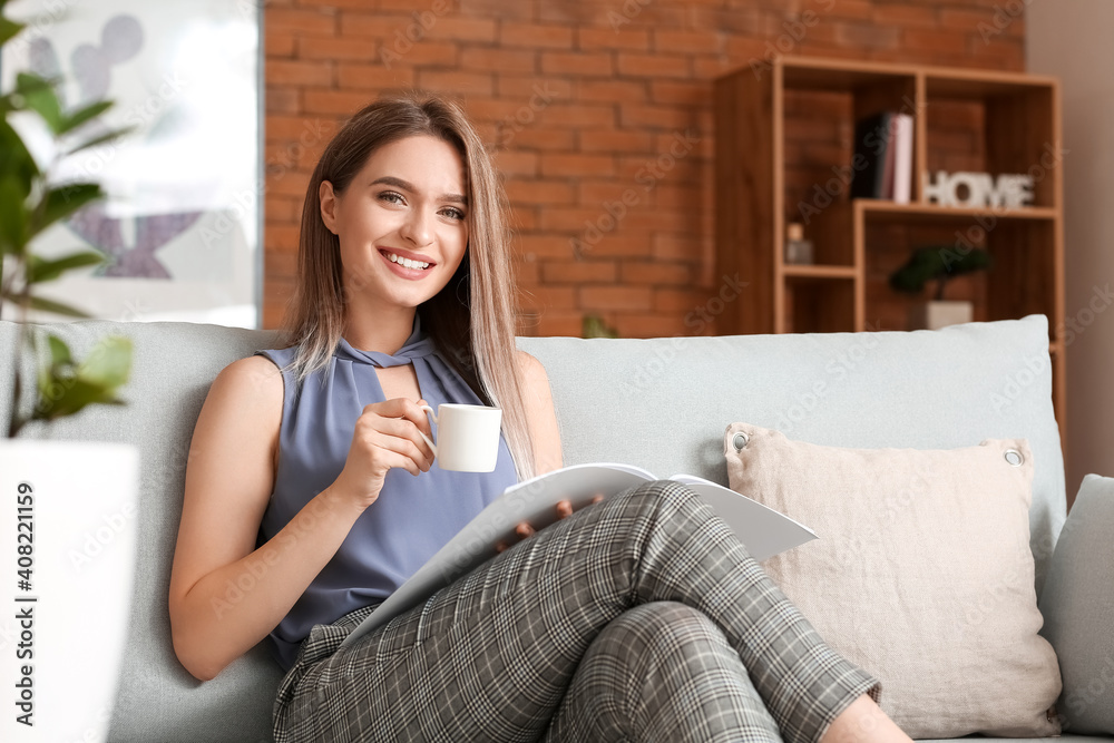 Beautiful woman with blank magazine and drinking coffee in living room