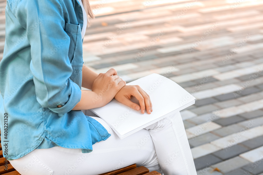 Young woman reading blank magazine in park