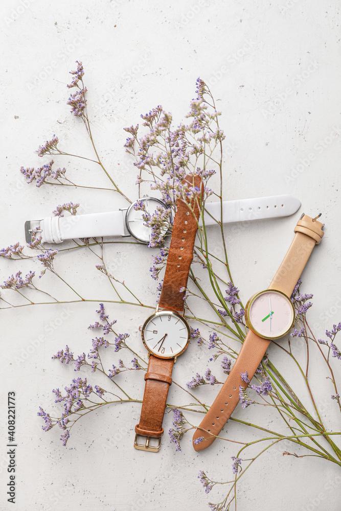 Stylish wristwatches and flowers on light background