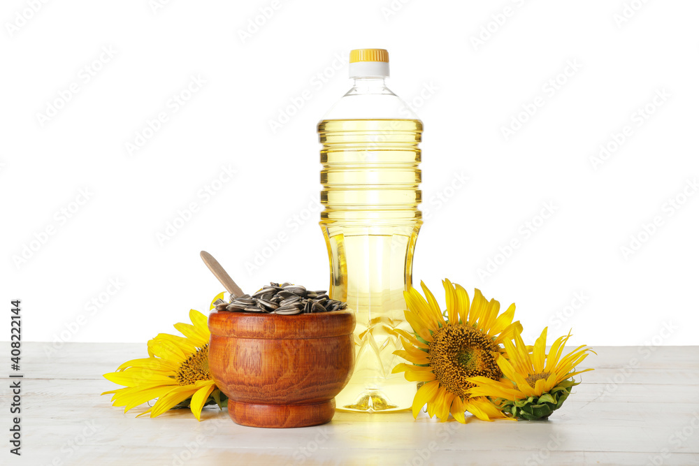 Bottle of oil, bowl with seeds and sunflowers on table against white background