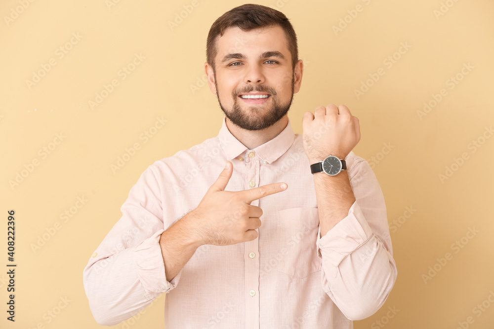 Handsome man pointing at wristwatch on color background