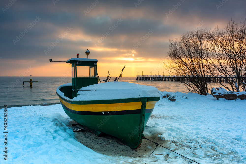 Fishing boat on snowy beach in Gdynia Orlowo at sunrise, Baltic Sea. Poland