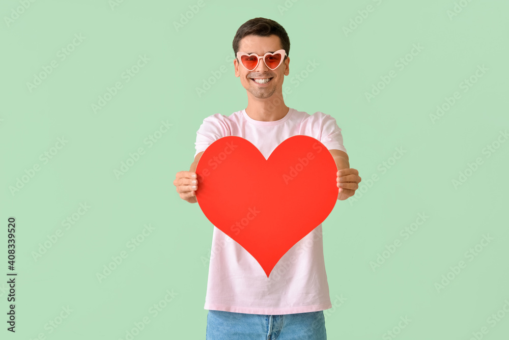 Handsome man with big red heart on color background