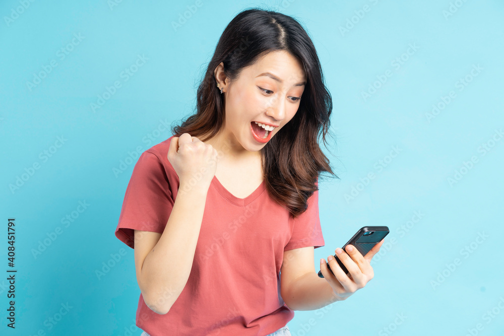 The beautiful Asian woman is looking at her phone and showing a triumphant expression