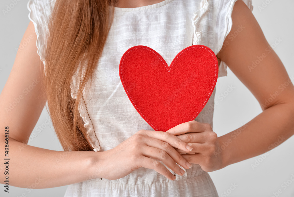 Young woman with red heart on grey background, closeup