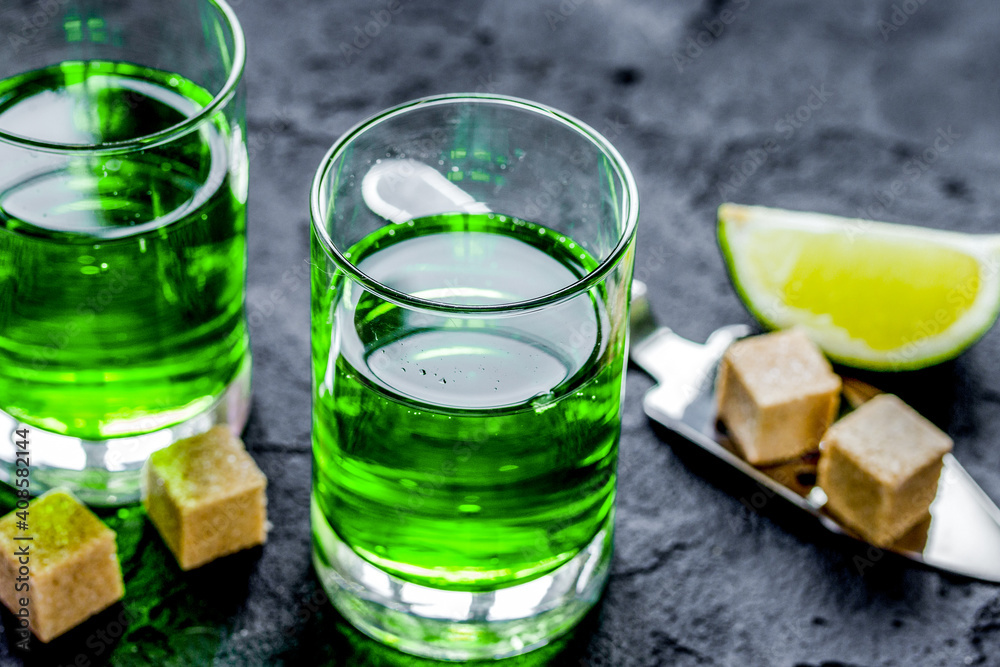 absinthe with sugar cubes in spoon on dark background