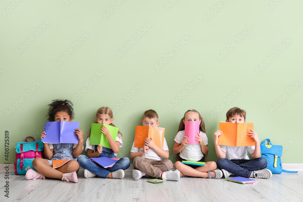 Little children with books sitting on floor against color background