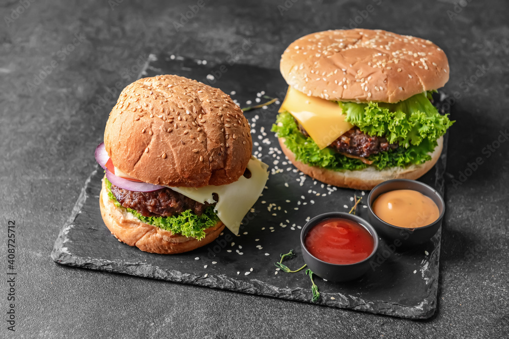 Board with tasty burgers and sauces on dark background