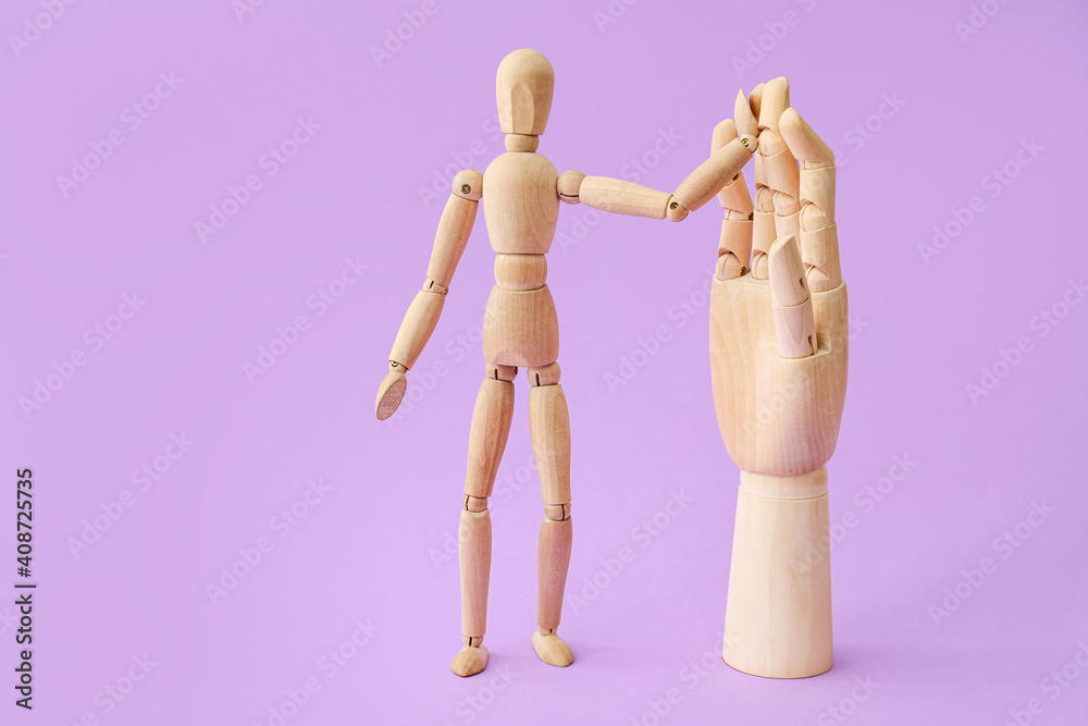 Wooden mannequin and hand on color background