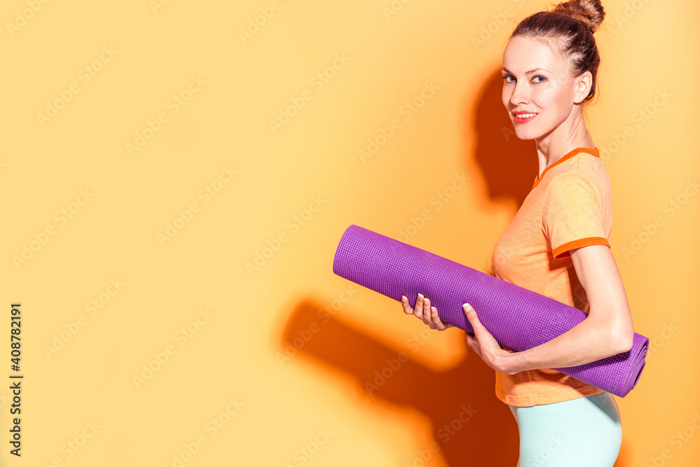 Sporty yoga girl with yoga mat isolated over yellow orange background	