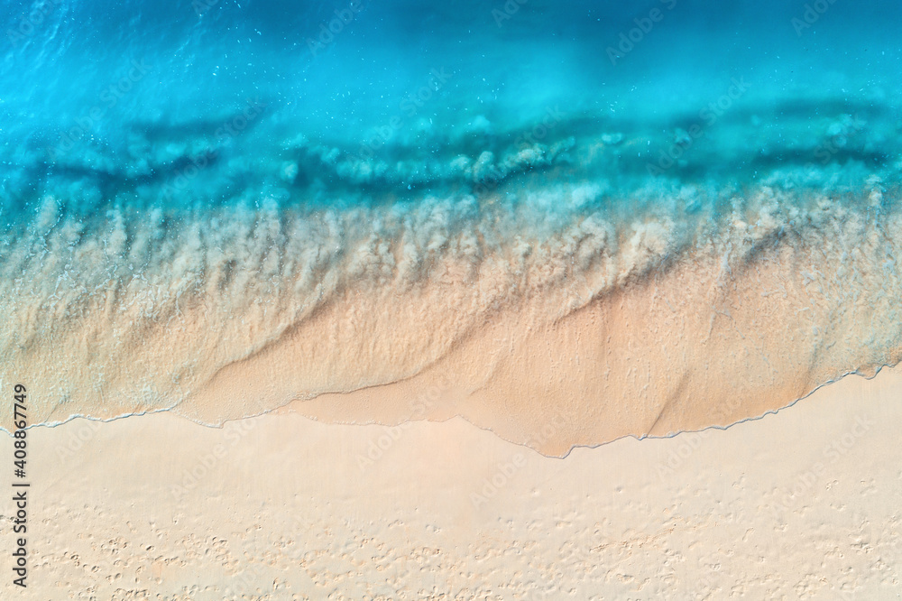 Aerial view of clear blue sea with waves and empty white sandy beach at sunset. Summer in Zanzibar, 