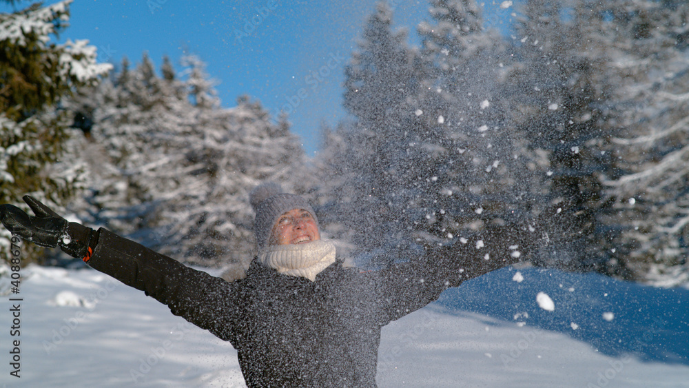 CLOSE UP: Joyful female tourist throws a handful of fresh snow in the air.