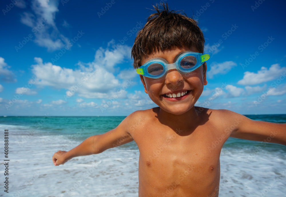 Close portrait of small boy in swimming googles stand on the beach