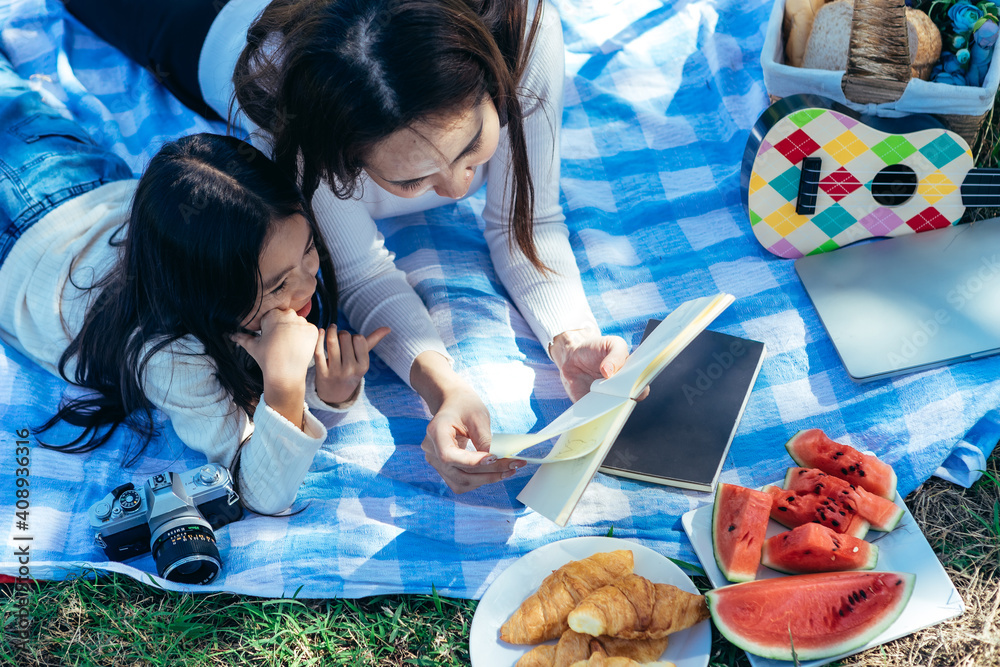 happy Asian family mom and daughter having a picnic in the garden and teaching their daughter to do 