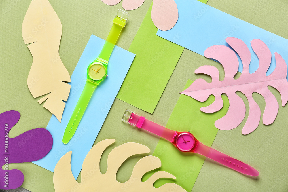 Composition with stylish wrist watches with paper tropical leaves on color background