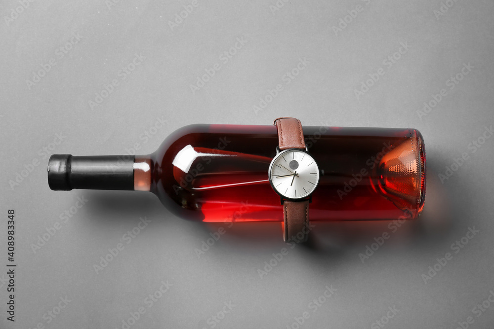 Stylish wrist watch and bottle of wine on gray background