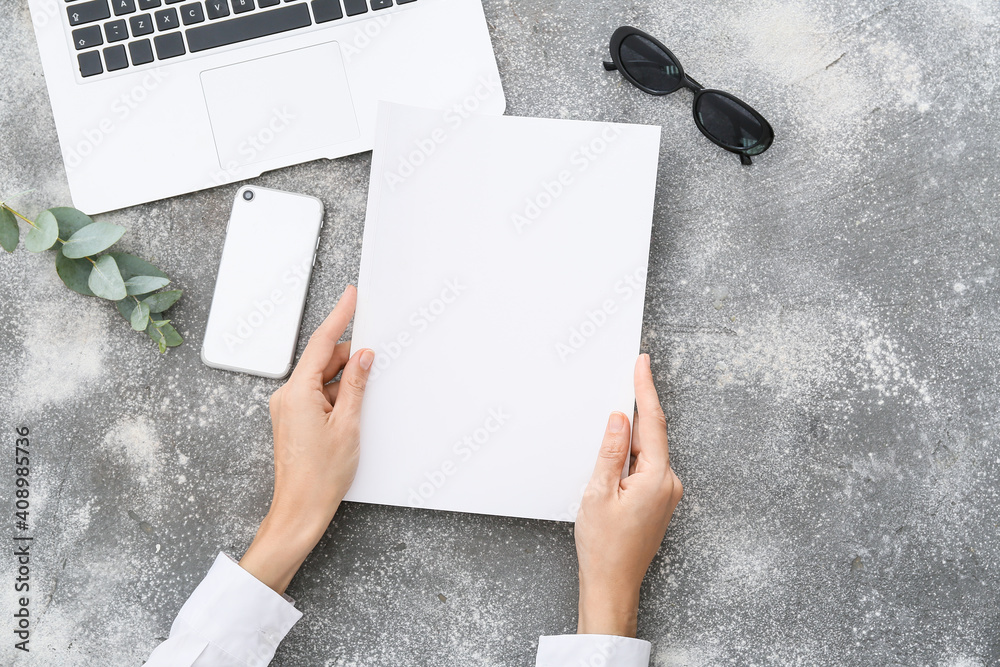 Female hands, blank magazine, laptop and mobile phone on grey background